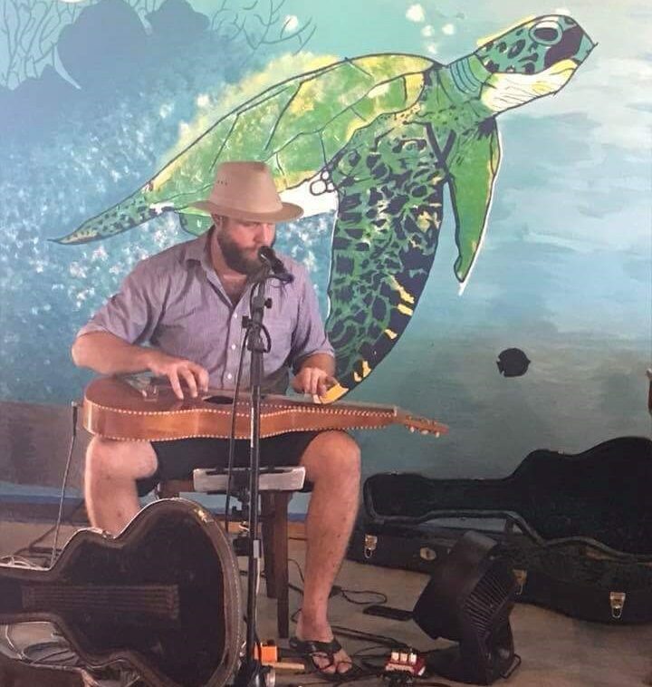 A man playing an instrument in front of a mural.