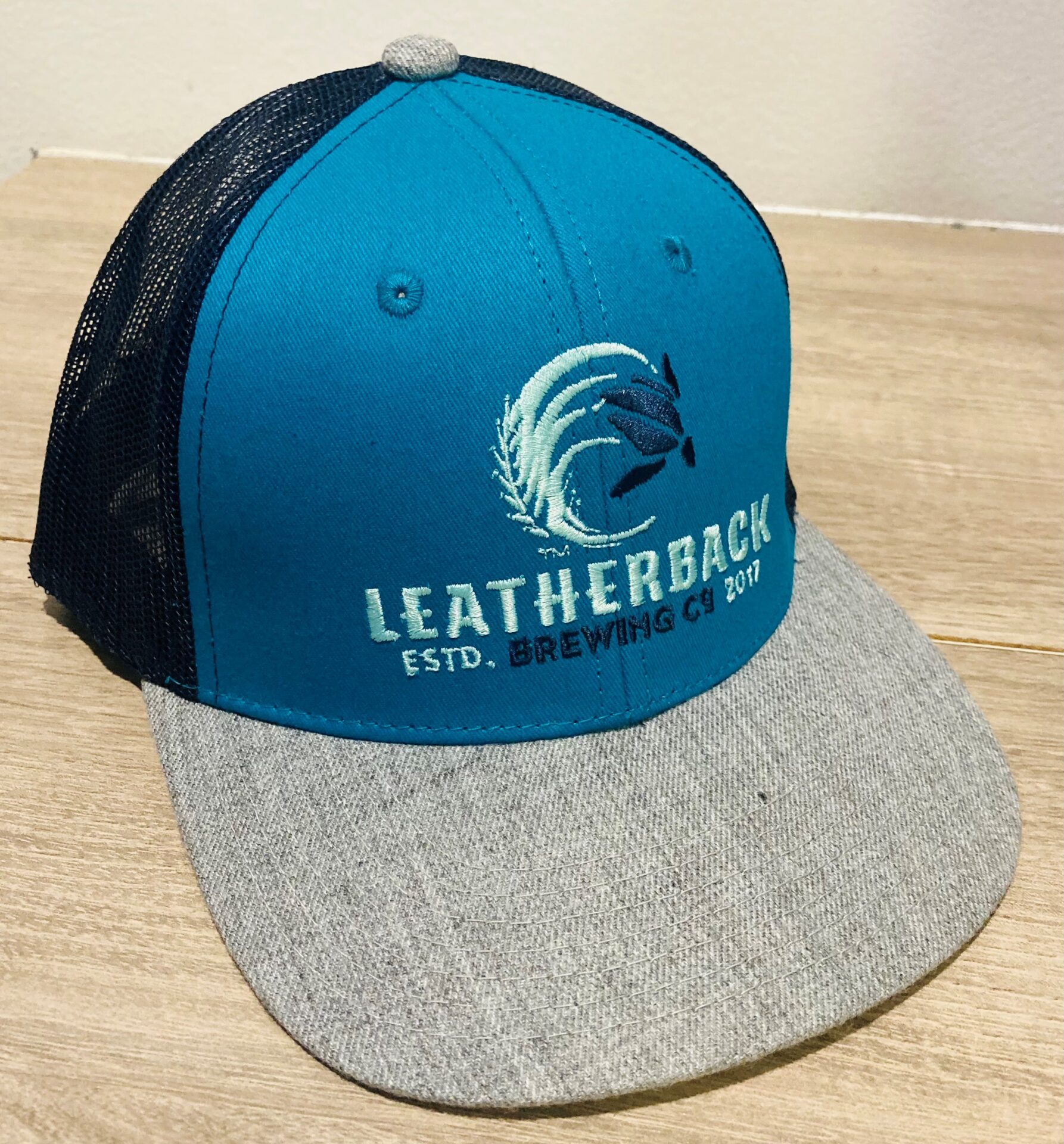 A blue and grey hat with the words " leatherback."